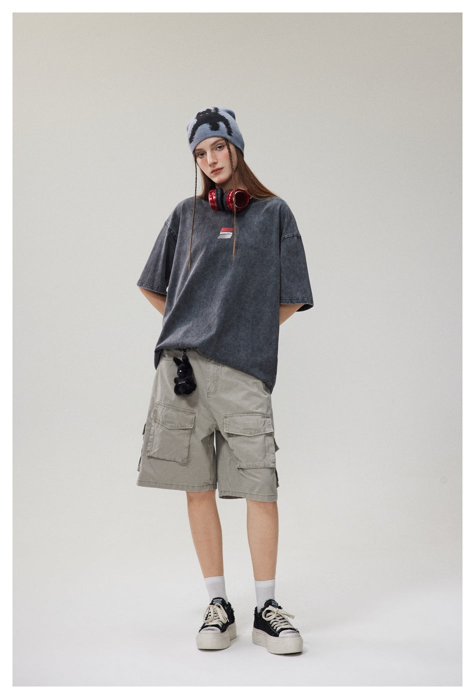 Model wearing an oversized faded charcoal T-shirt with a small chest graphic and light gray cargo shorts.