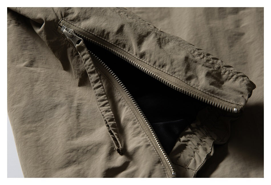 Close-up of an olive-brown jacket with a partially open zipper pocket and fabric pull tab.