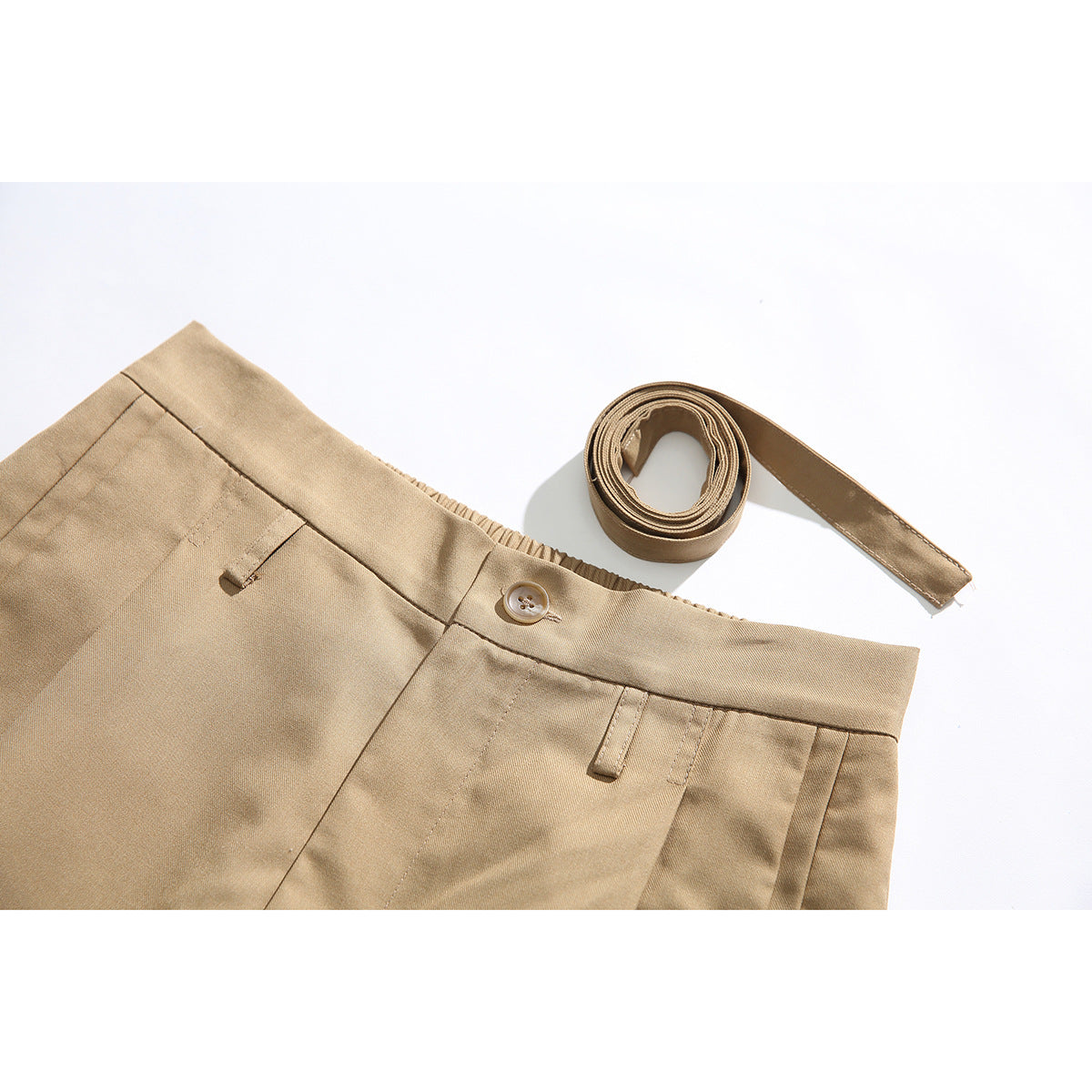Close-up of tan shorts showing the waistband, button, belt loops, and a matching rolled belt.