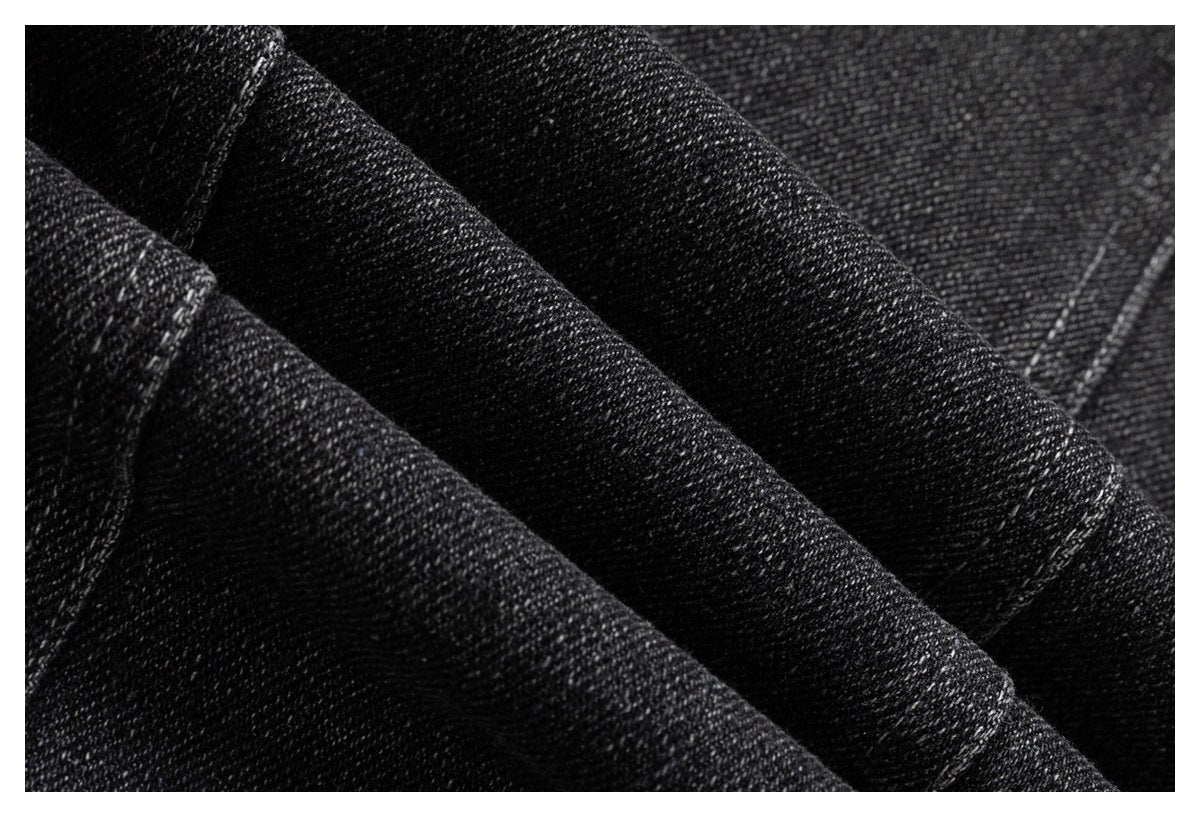 Macro view of dark charcoal denim fabric showing its diagonal weave and subtle pale flecks.