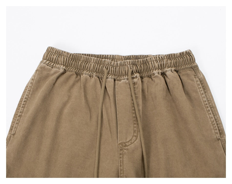 Close-up of tan pants showing the gathered elastic waistband, drawstring, pleats and front pocket openings.