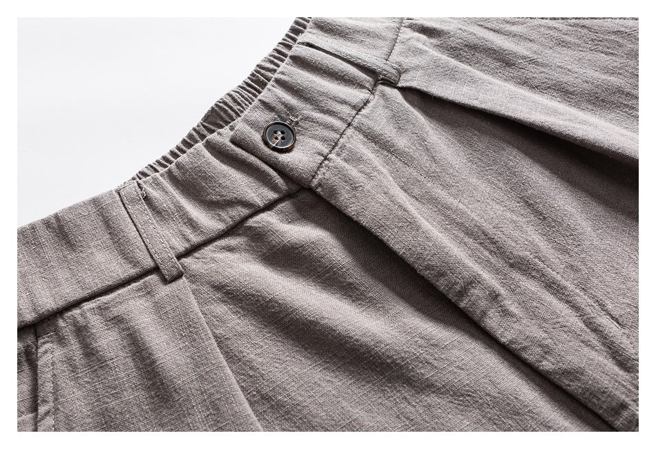 Close-up of light gray trousers showing the buttoned waistband, belt loop, and front fly.