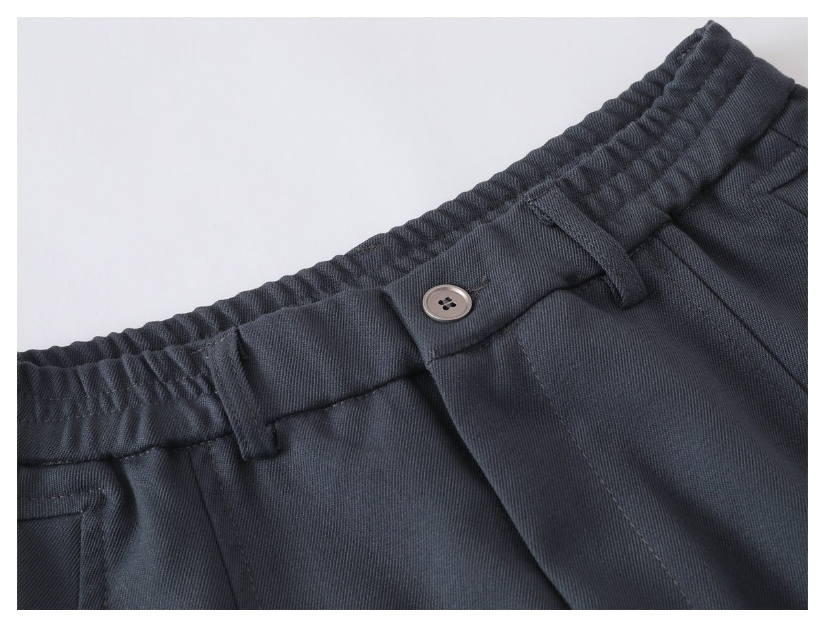 Close-up of charcoal trousers showing an elastic waistband, belt loops, and button closure.