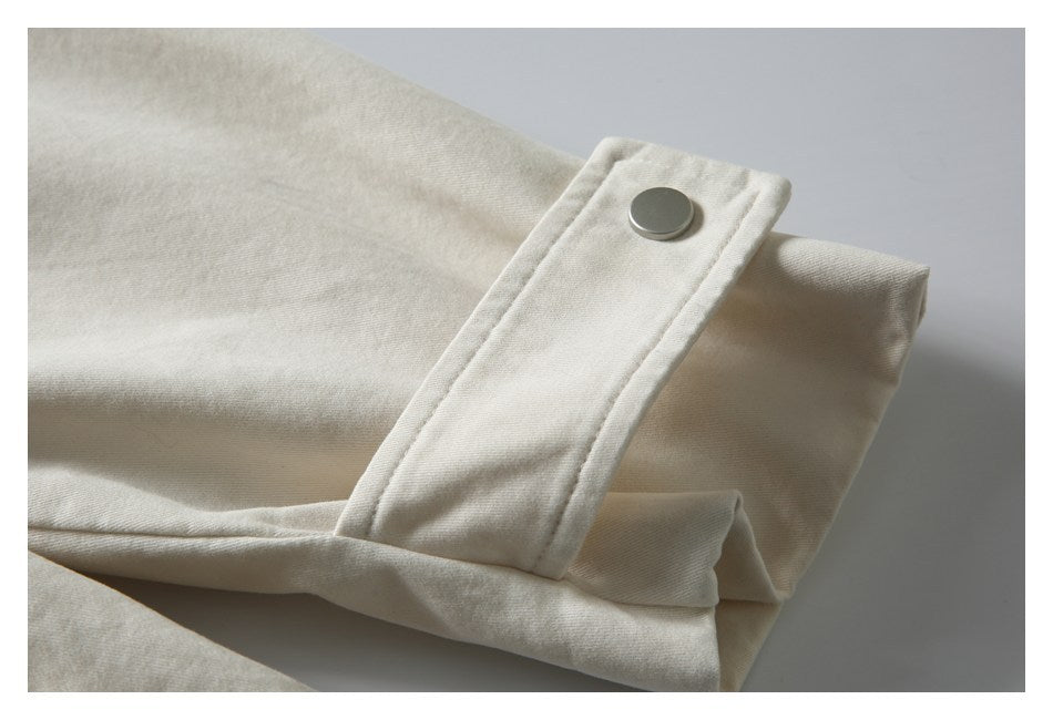 Close-up of an ivory fabric tab with a round metal snap over a folded garment edge.