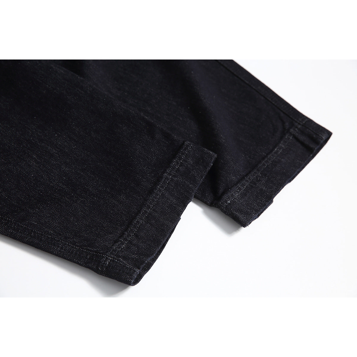 Close-up of the stitched hems of black denim trouser legs.