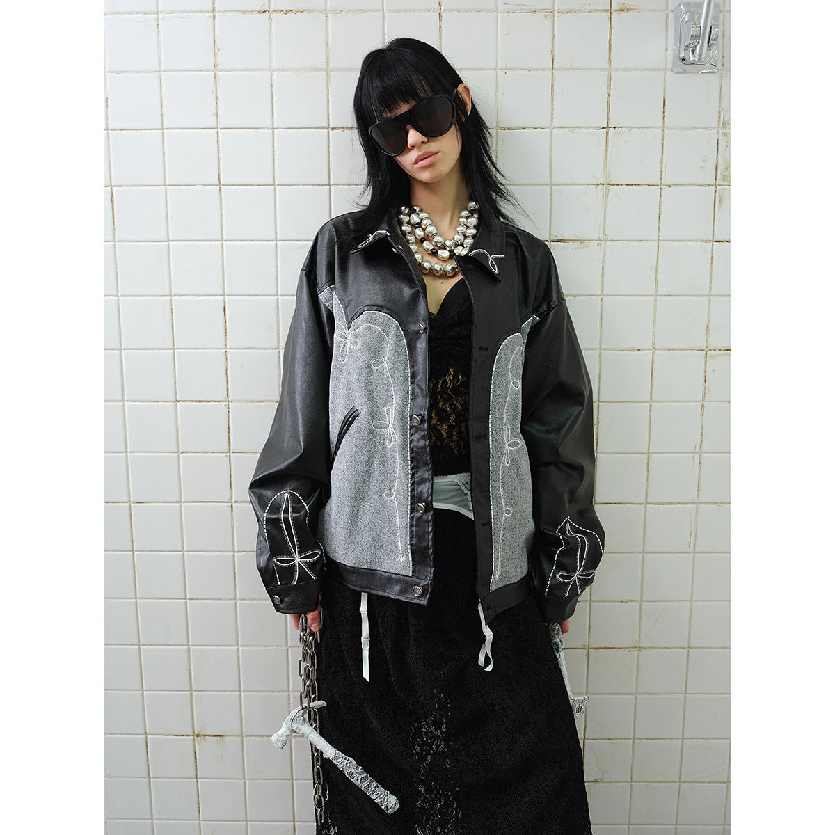 Closer view of a model wearing a black jacket with gray panels, white decorative stitching, and a button front.