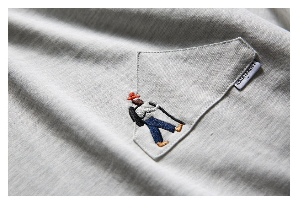 Close-up of a light gray T-shirt pocket with small embroidered figures and a sewn label.