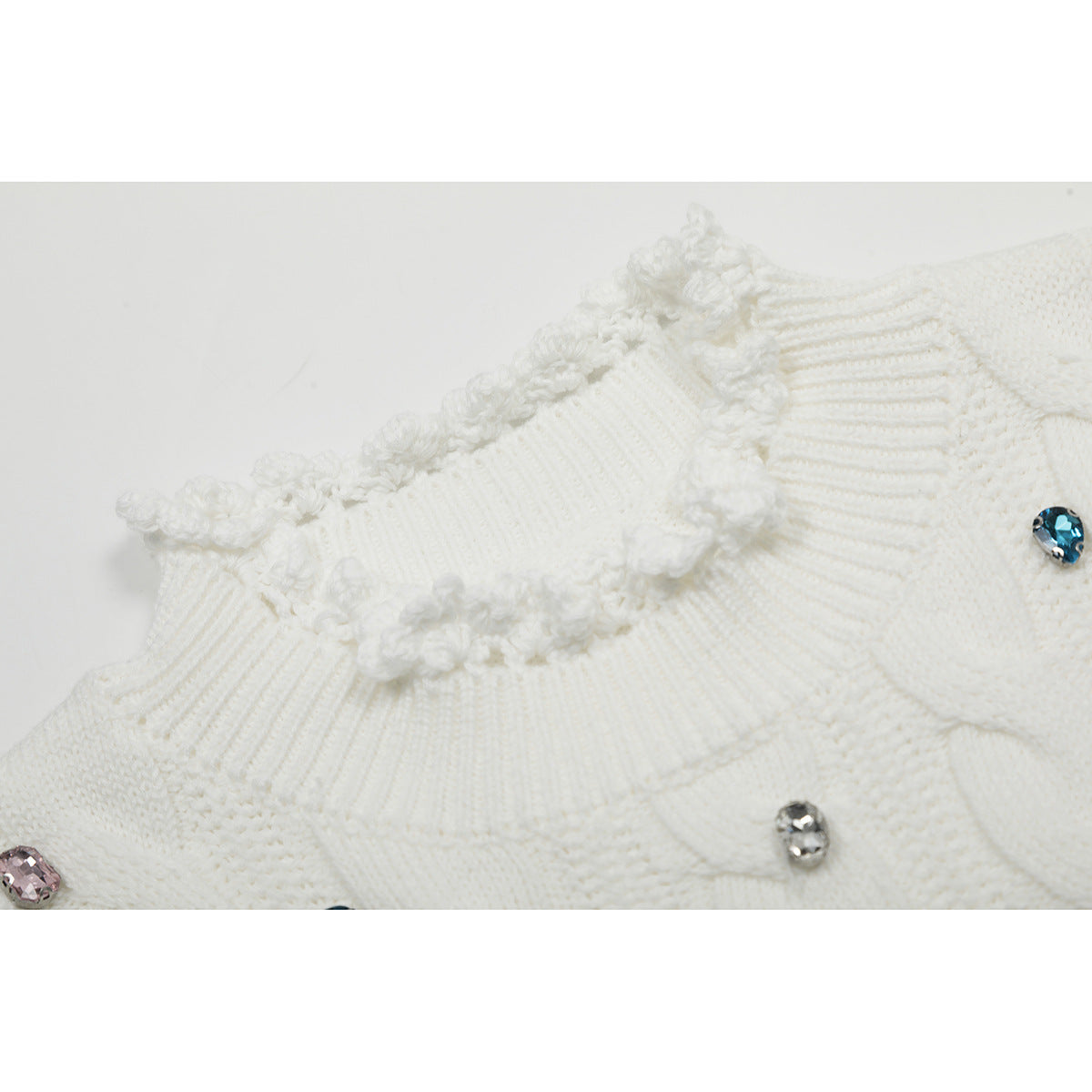 Close-up of a white sweater's ruffled ribbed neckline and colorful jeweled embellishments.