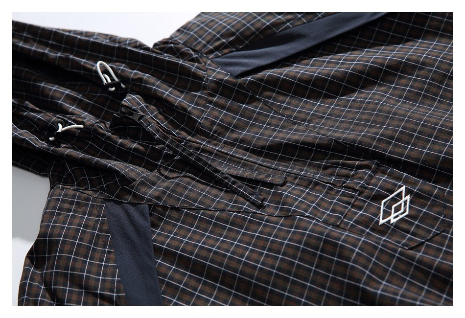 Close-up of dark plaid garment fabric with white drawcords, black trim and a small white geometric emblem.