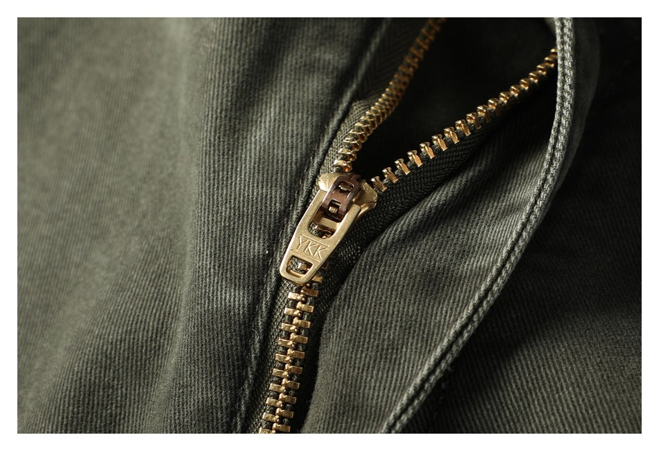 Close-up of the pants' open gold-tone zipper and dark olive-gray fabric.