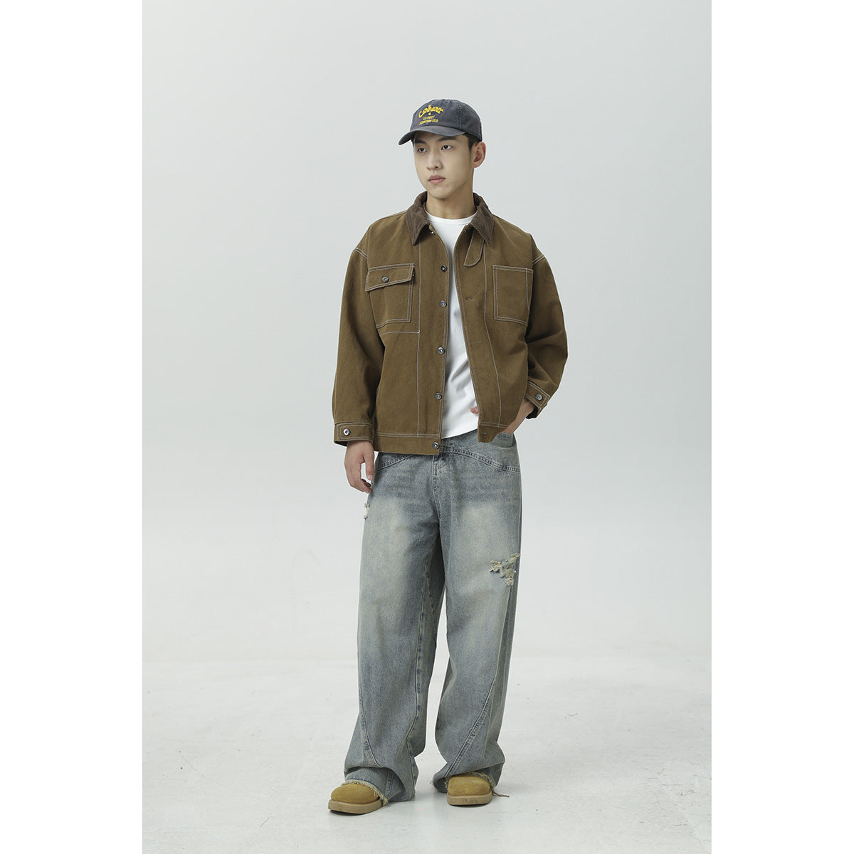 Full-length view of a model wearing a brown work jacket with contrast stitching and two chest pockets.