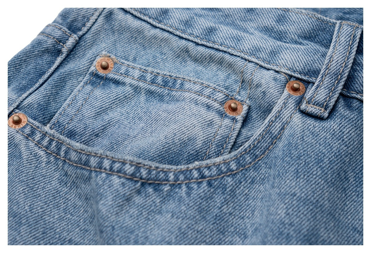 Close-up of a light blue denim front pocket with copper-colored rivets and tan stitching.