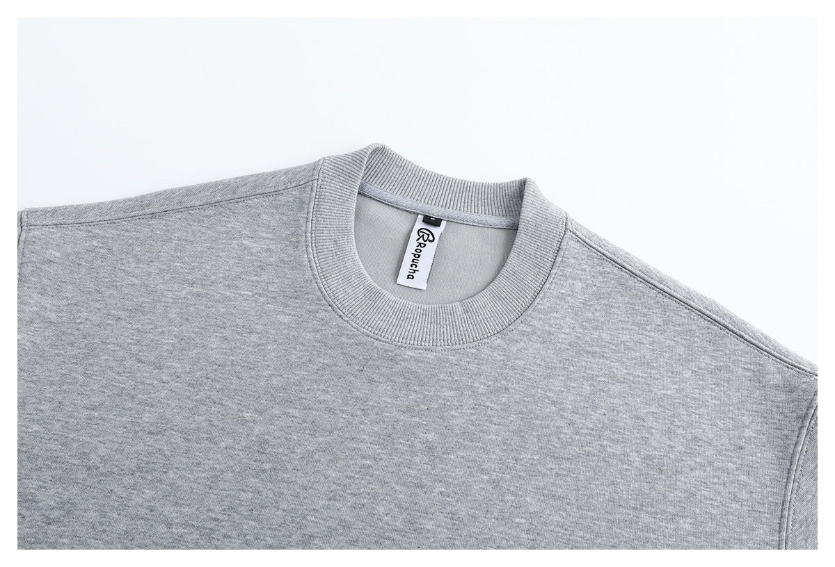 Close-up of a light gray sweatshirt's ribbed crew neck, shoulder seams, and branded neck label.