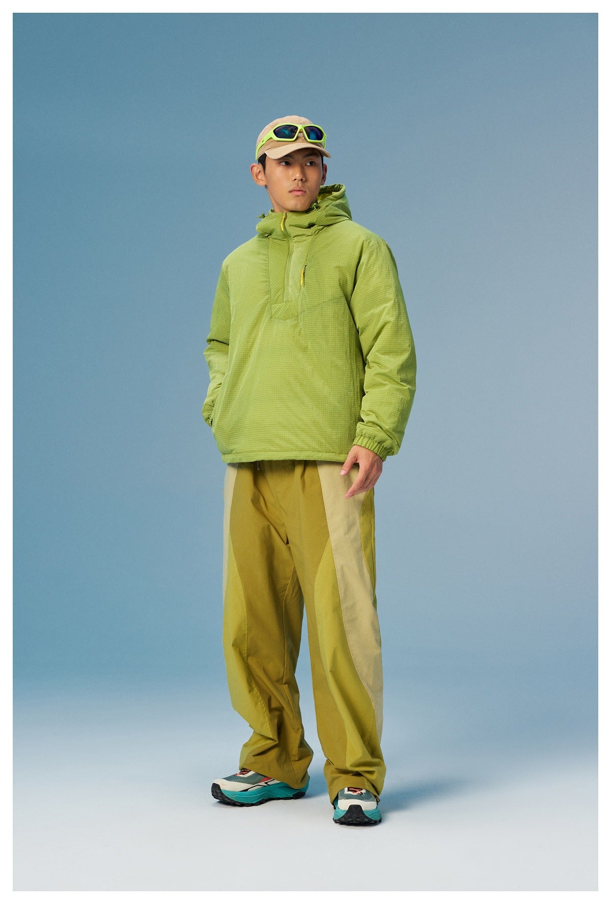 Model wearing a lime green grid-pattern hooded pullover with a yellow chest zipper and color-block trousers.