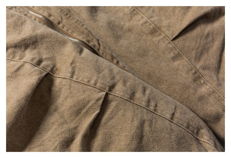 Close-up of a tan garment showing a metal zipper and overlapping stitched panels.