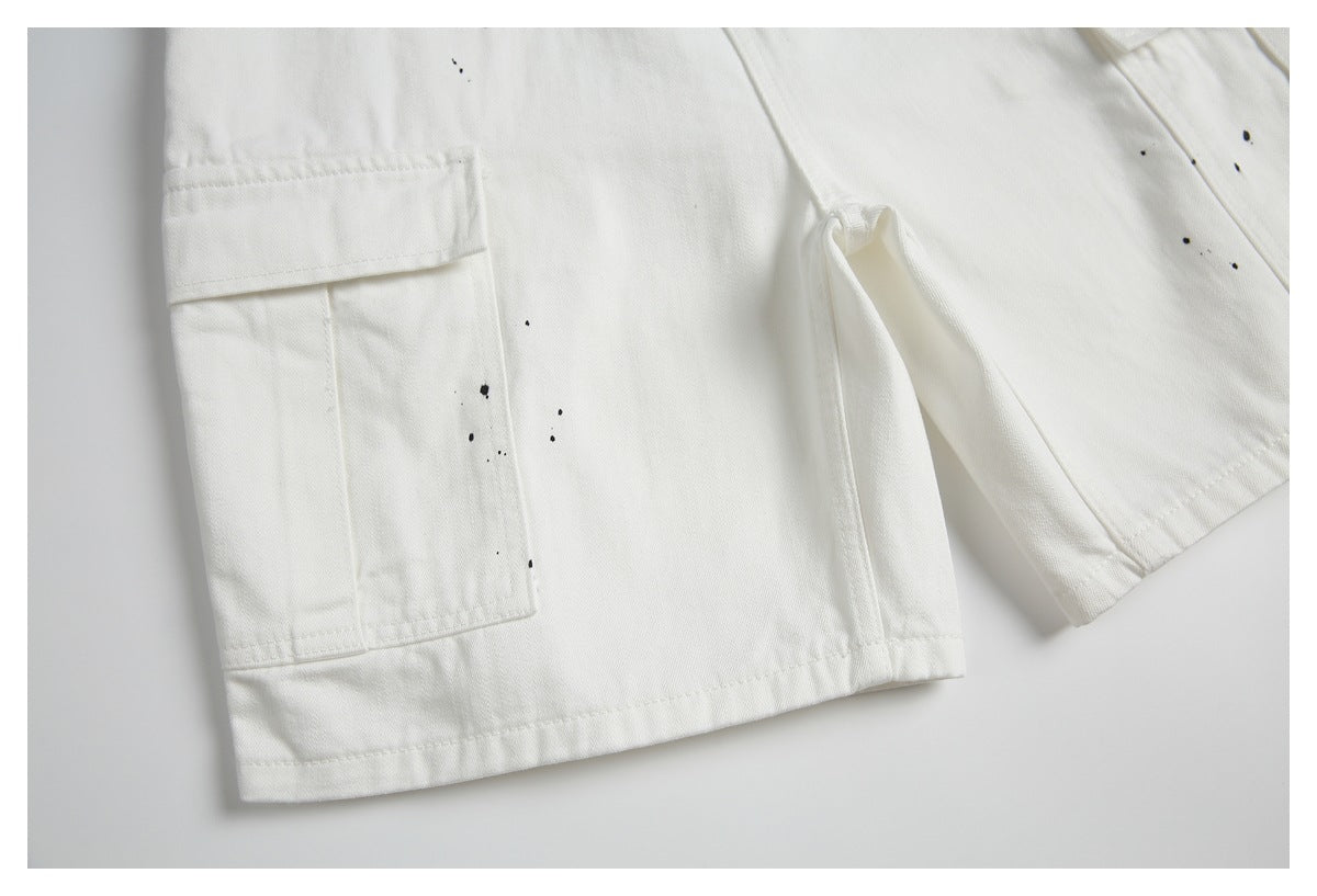 Close-up of off-white shorts with a flap cargo pocket, hem stitching, and scattered black paint-like marks.