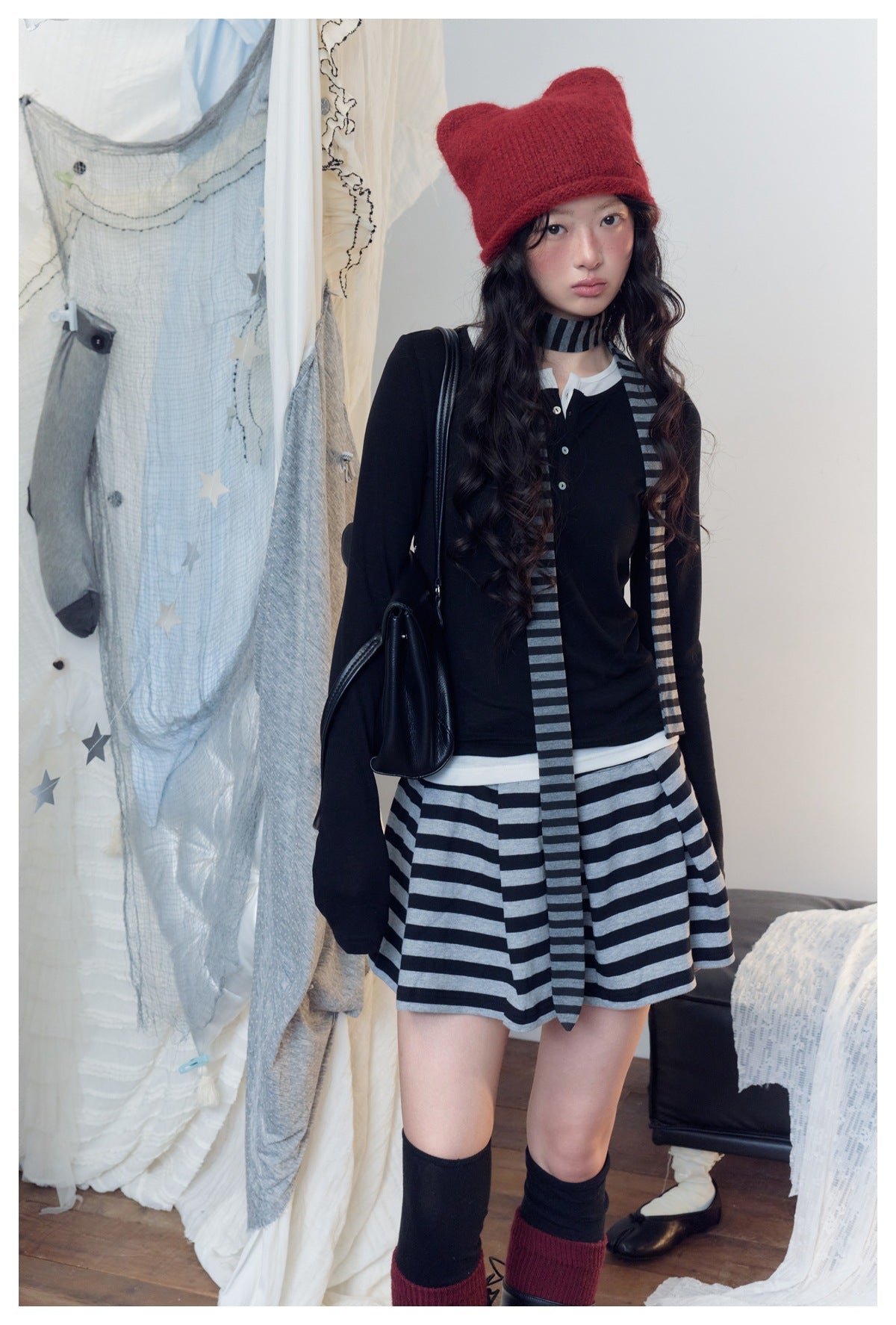 Model wearing a black button-front top, gray-and-black striped mini skirt and scarf, and a red knit hat.