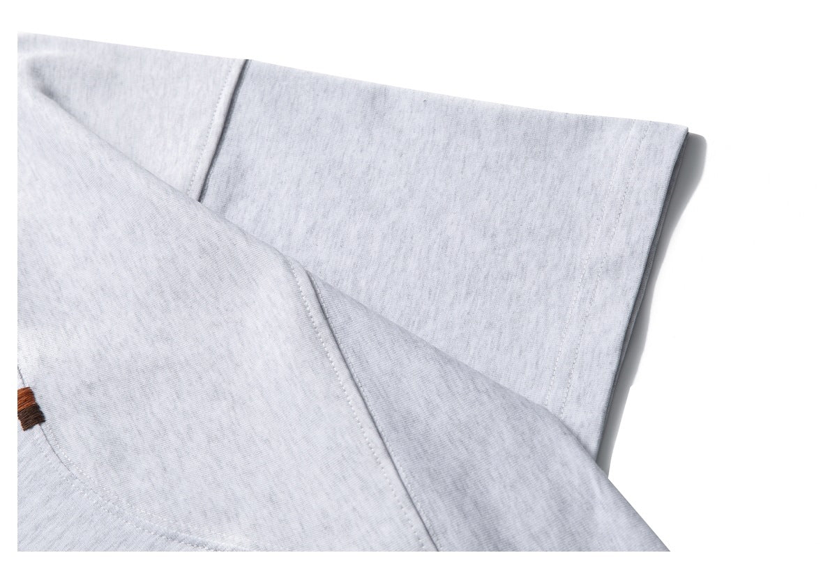 Close-up of light gray knit garment fabric with a seam and a small brown stitched accent.