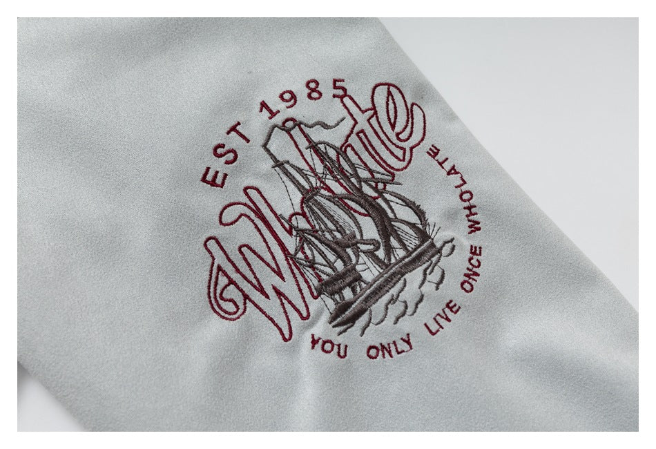 Close-up of burgundy and gray embroidered ship artwork with English lettering on light gray fabric.