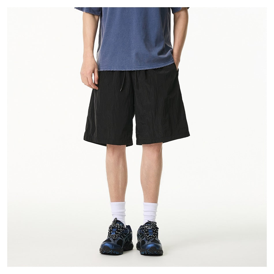 Front view of a model wearing loose black knee-length shorts with a drawstring and pockets.