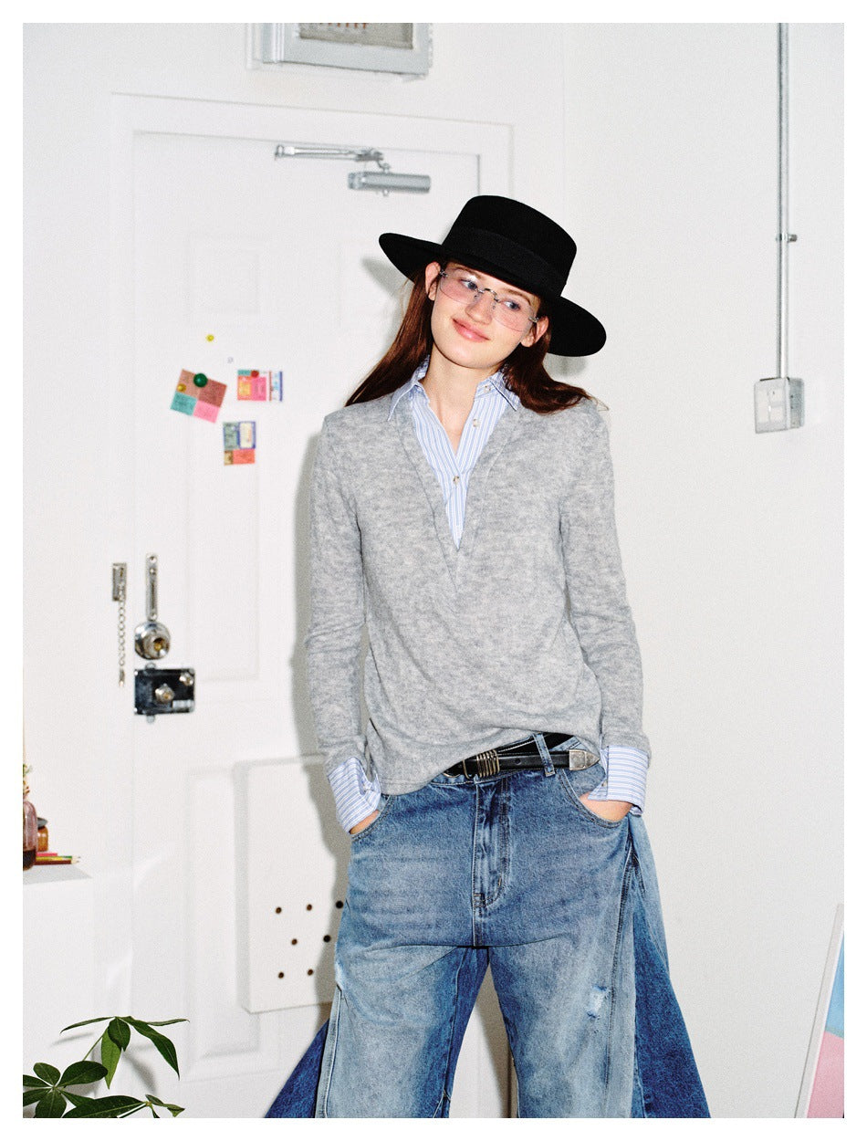 Model wearing a light gray V-neck sweater over a blue striped shirt with wide-leg jeans and a black hat.