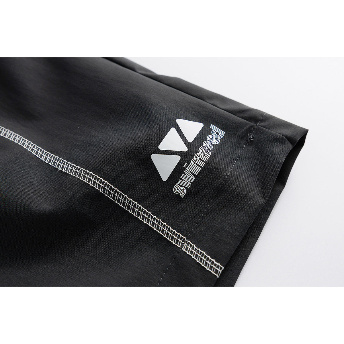 Close-up of black shorts showing white contrast stitching and a white printed logo near the hem.