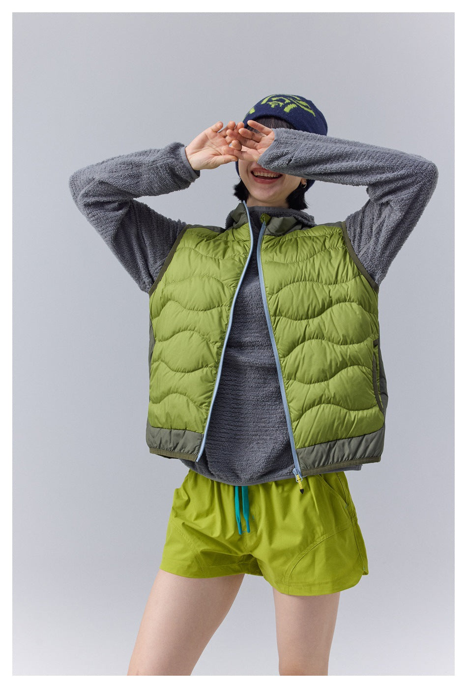 Model wearing an open lime-green wave-quilted vest over a gray fleece.