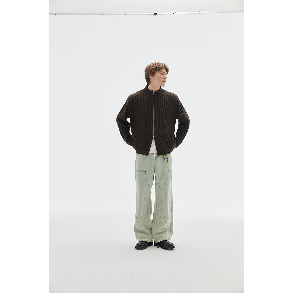 Full-length view of a model in a dark brown ribbed zip cardigan and pale green wide-leg jeans.