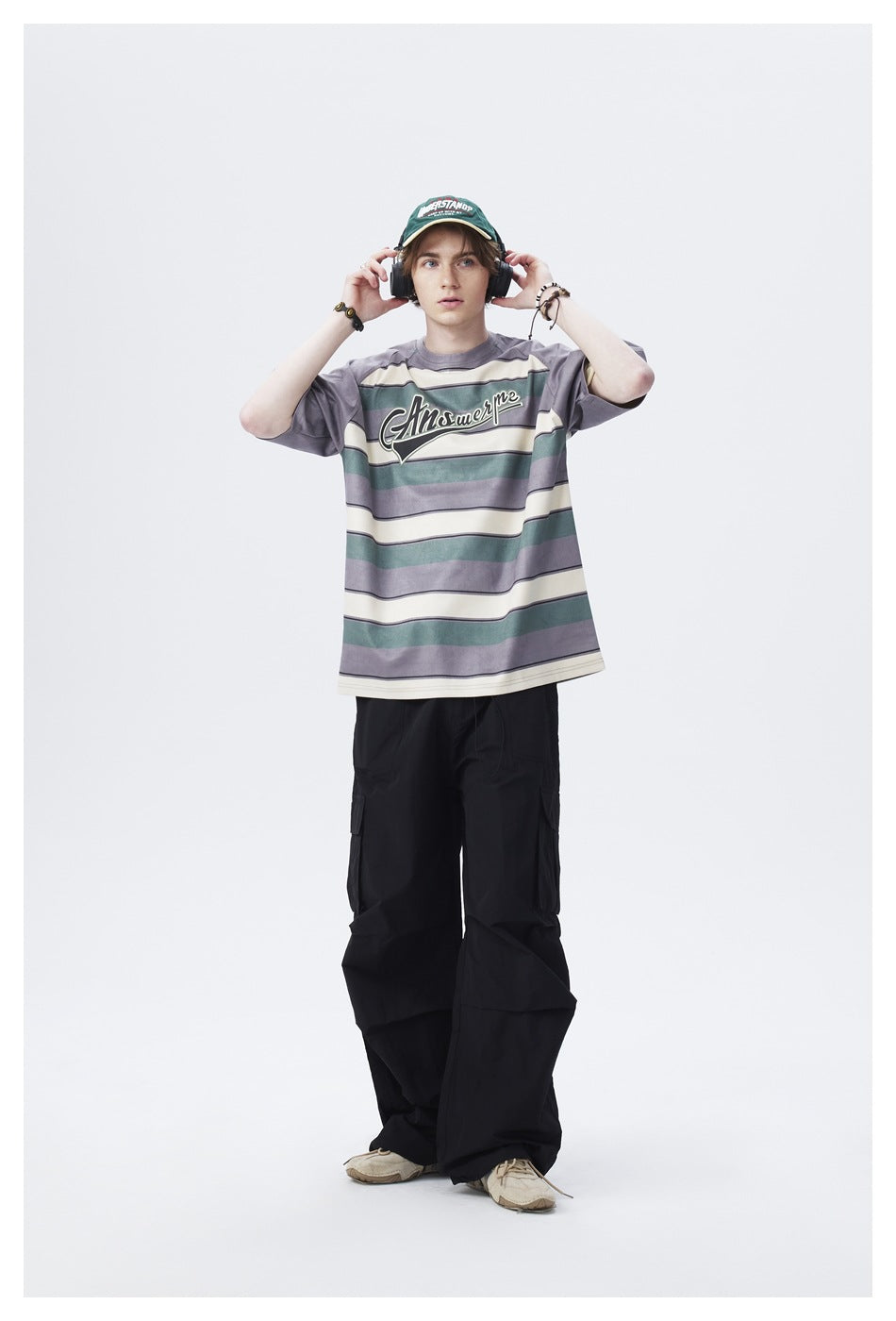 Model wearing gray striped raglan T-shirt with black cargo pants, hands on headphones, front view