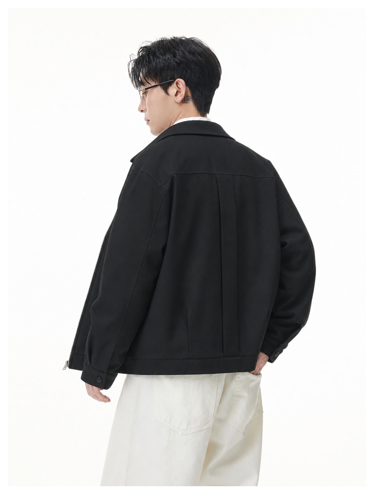 Model wearing a black jacket, shown from behind with a slight side profile and white trousers.