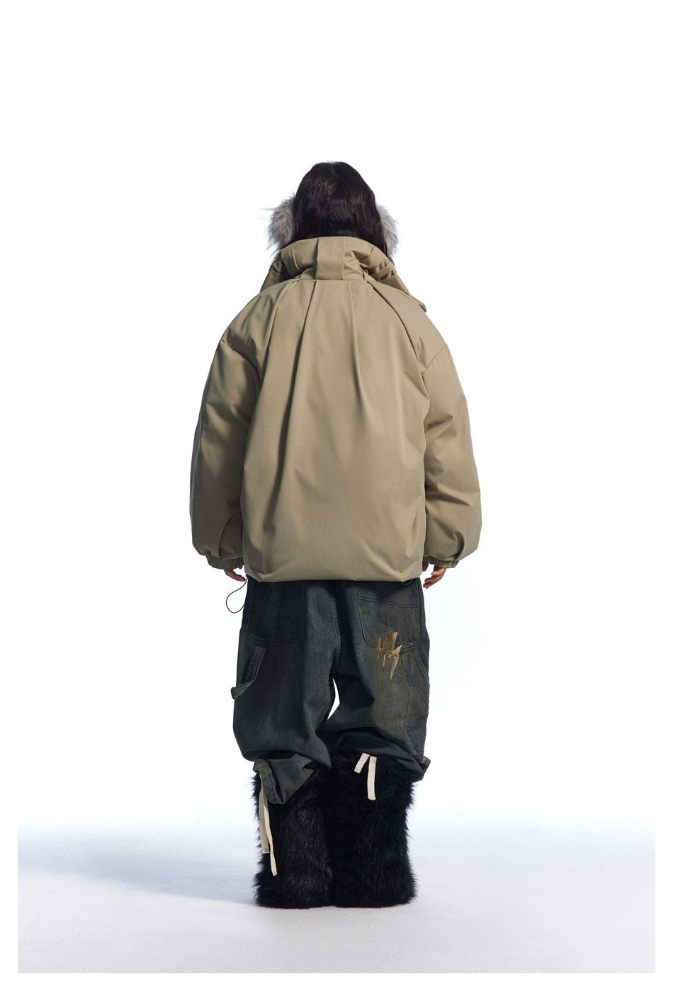 Rear view of a model wearing an oversized taupe hooded jacket with gray fur trim and dark loose-fit jeans.