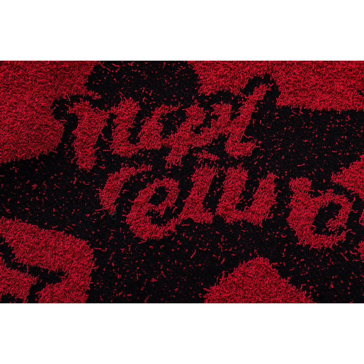 Close-up of a red and black shaggy scarf showing a large textured lettering pattern.