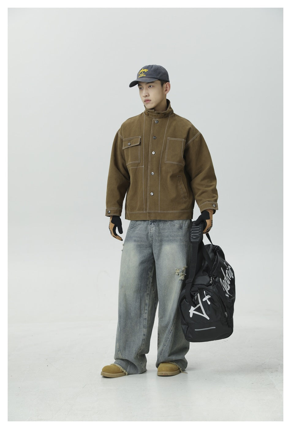 Full-length view of a model wearing a brown work jacket fastened to its stand collar, with contrast stitching and chest