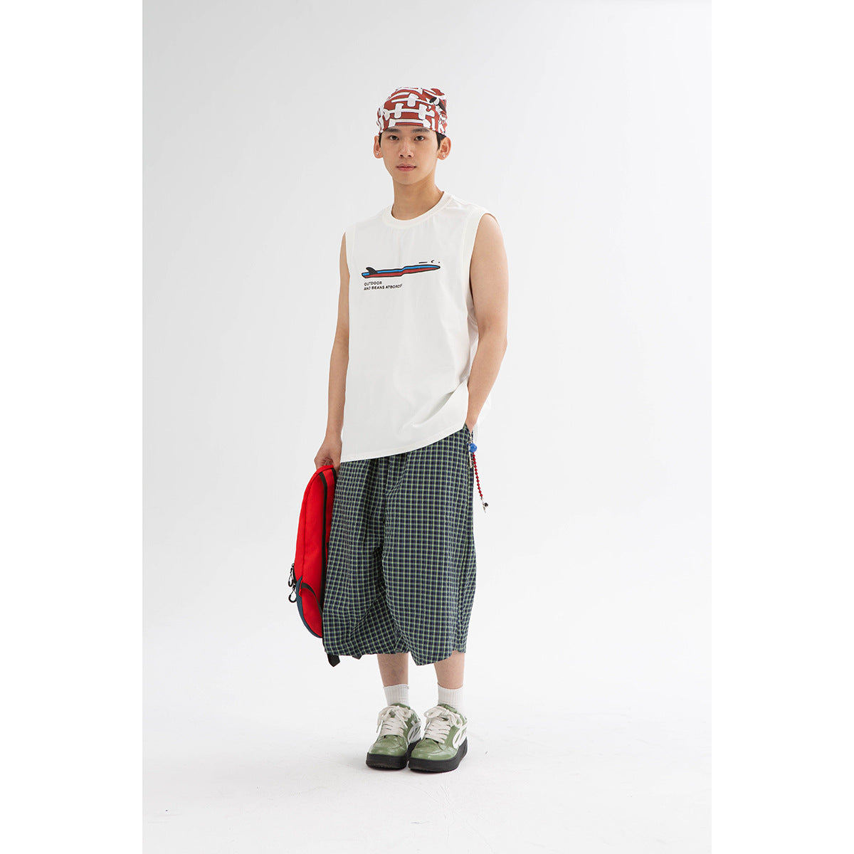 Model wearing a white graphic sleeveless shirt and loose navy-and-green plaid shorts, front view.