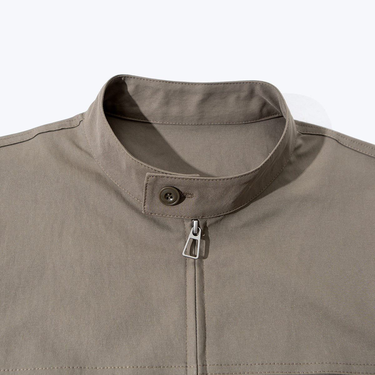 Close-up of a taupe jacket's stand collar, button tab, and front zipper.