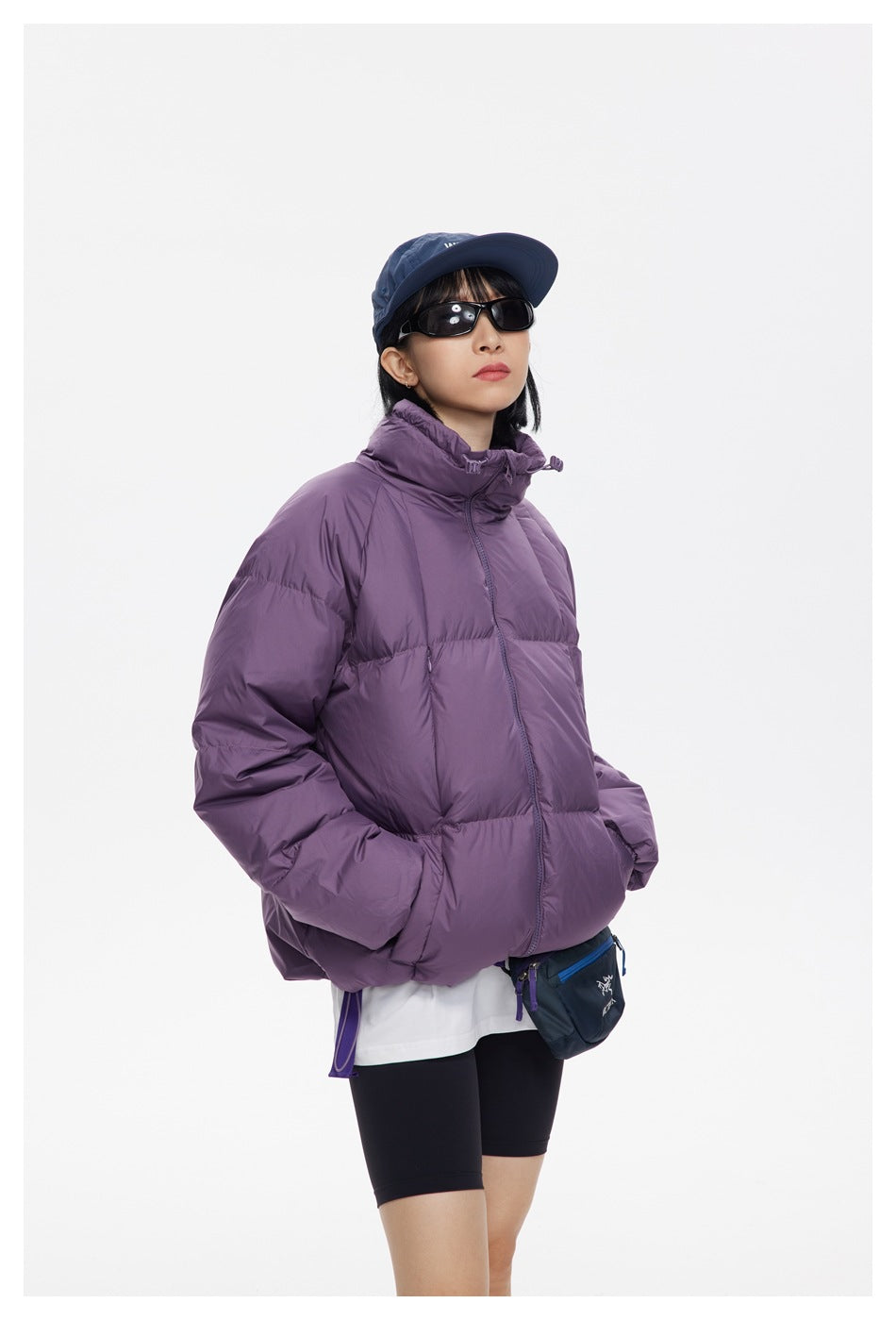 Model wearing a plum-purple quilted puffer jacket with a high collar and front zip, shown from a three-quarter angle.