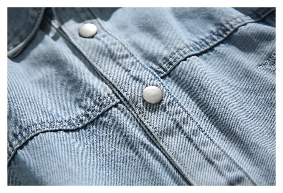 Close-up of light blue denim, metal snap buttons, topstitching, and a small embroidered mark.