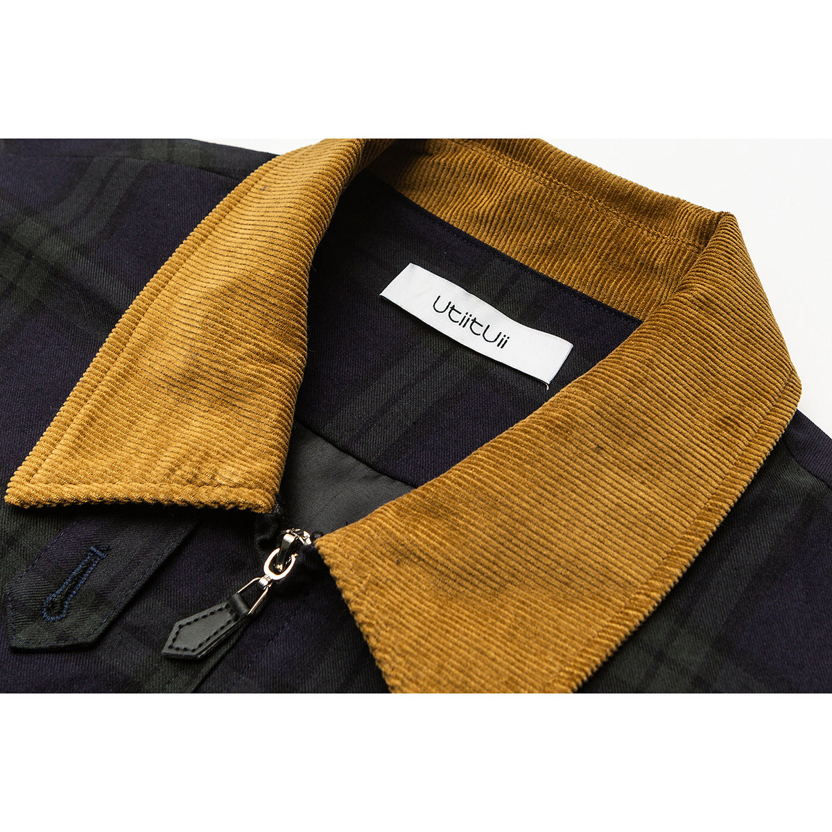 Close-up of a dark plaid jacket with a mustard corduroy collar, zipper pull, and white neck label.