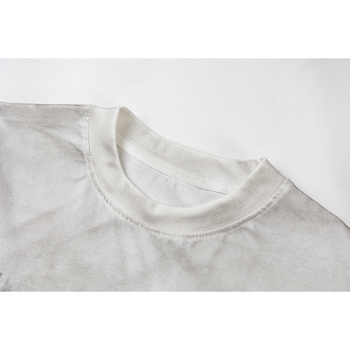Close-up of an off-white T-shirt's ribbed crew neck and shoulder seams.