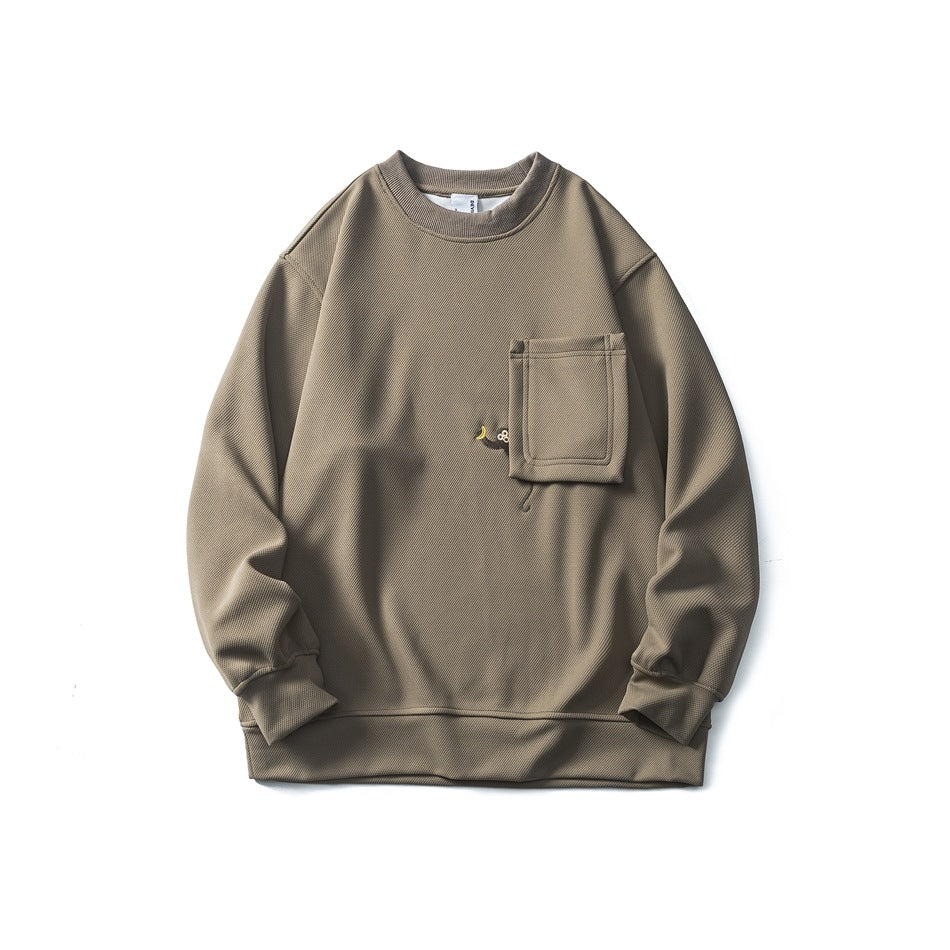 Light brown crewneck sweatshirt flat lay with chest patch pocket and small embroidered motif