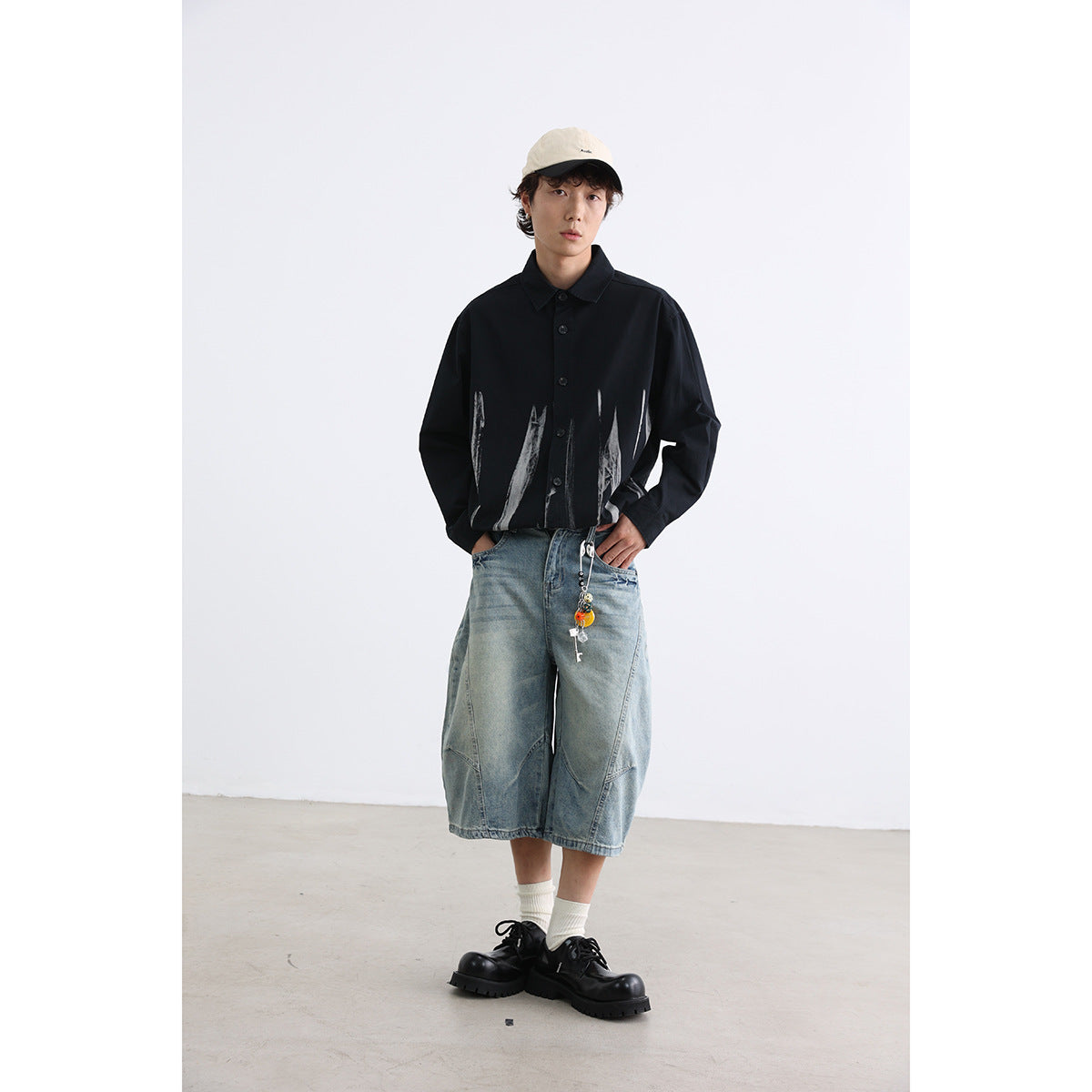 Model wearing a black button-up shirt with abstract white brushstroke graphics and denim shorts.