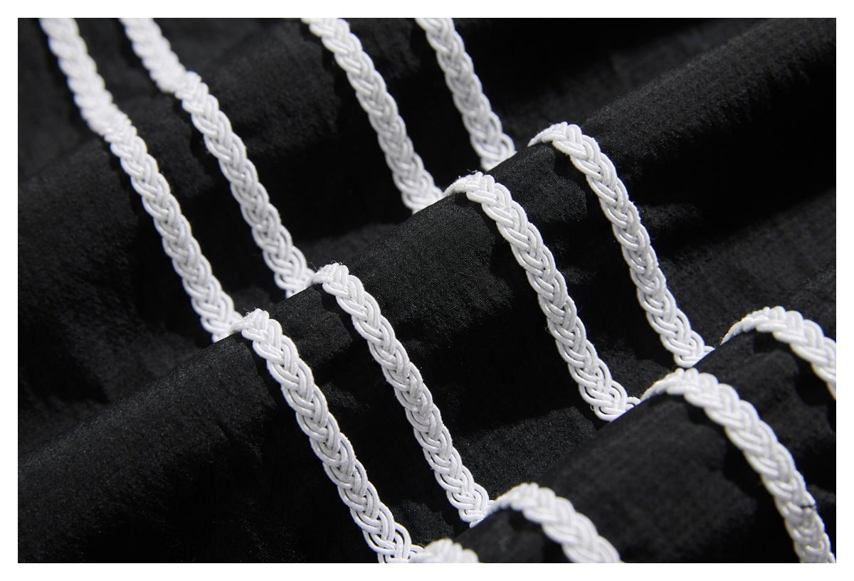 Close-up of black fabric with repeated white braided trim running across it.