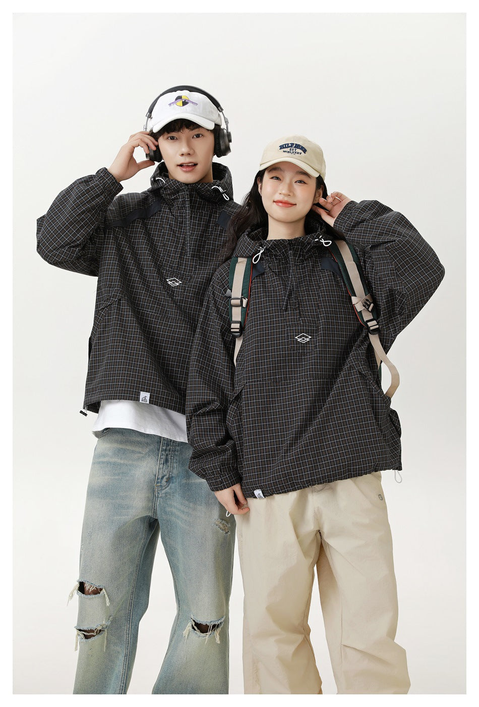 Man and woman wearing matching black checked hooded pullover jackets with front pockets and drawstrings.