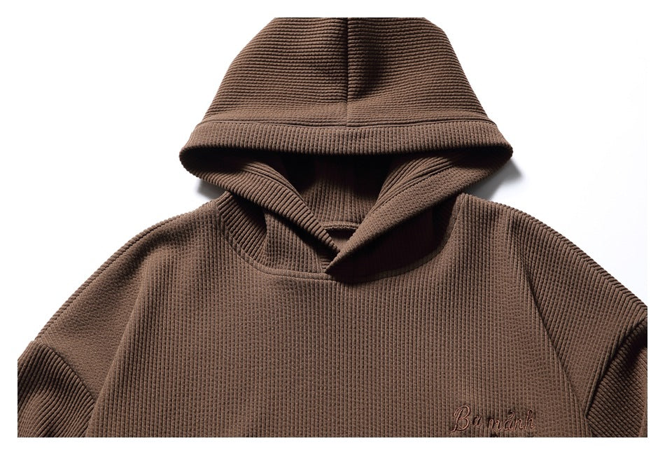Close-up of the brown hoodie’s hood and upper front, including small embroidered chest lettering.