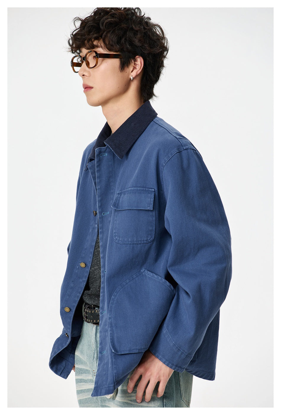 Side-front view of a model wearing a blue work jacket with a dark collar and large front pockets.