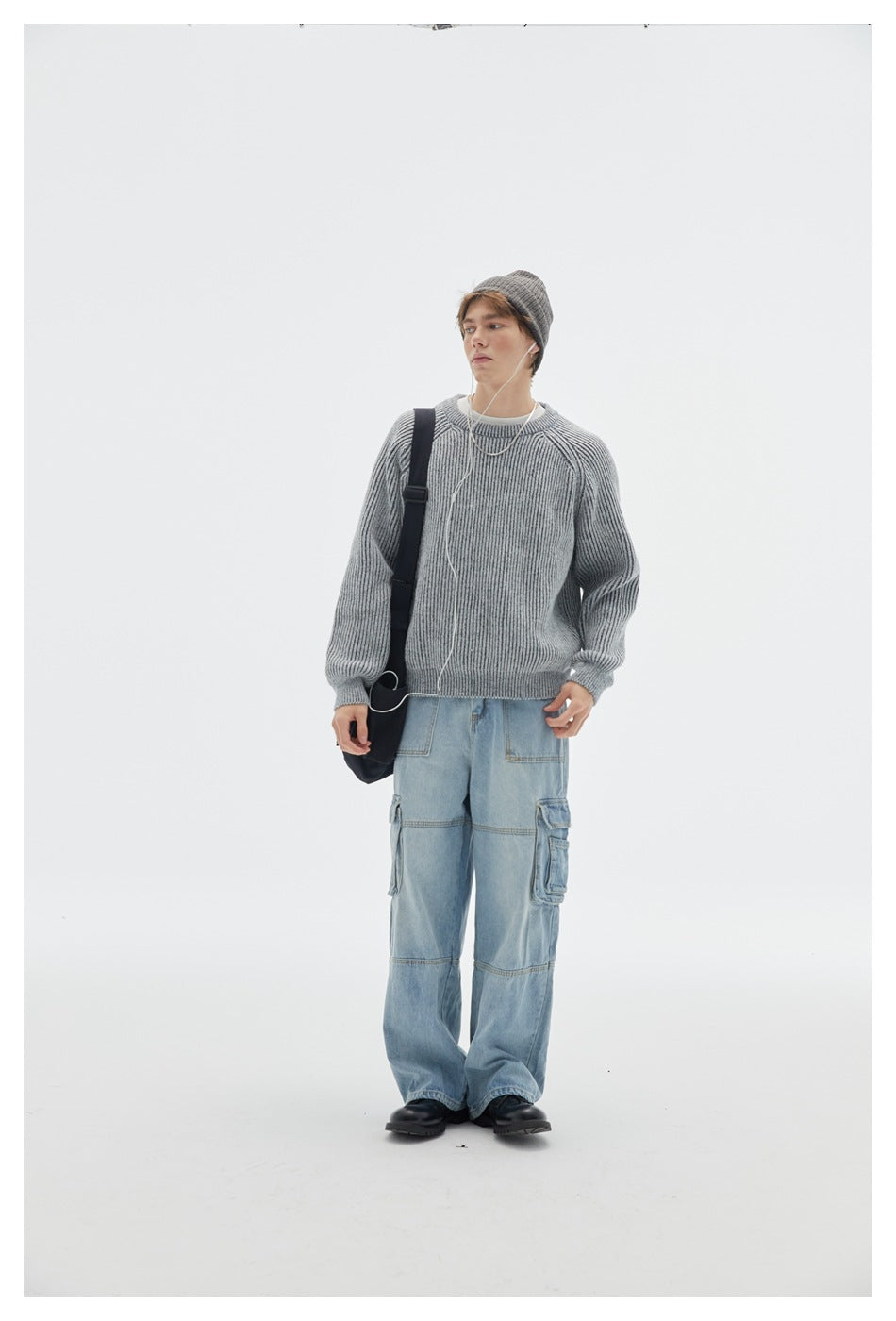 Full-length model wearing a light gray ribbed raglan sweater with a beanie, blue cargo jeans, and a black shoulder bag.