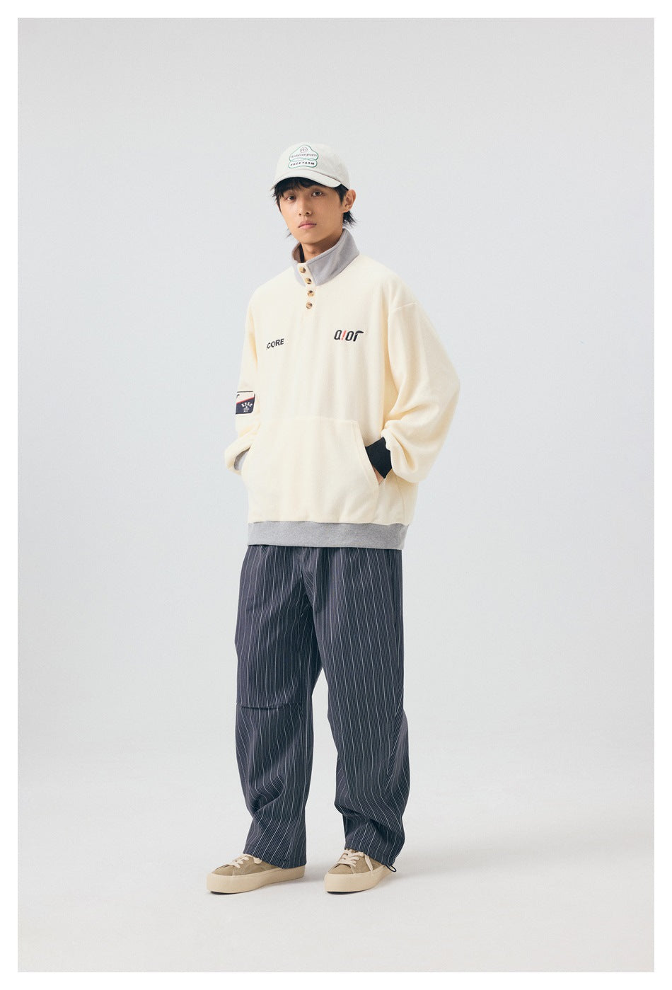 Model in the off-white pullover with hands in the front pocket, angled view, with striped pants and sneakers