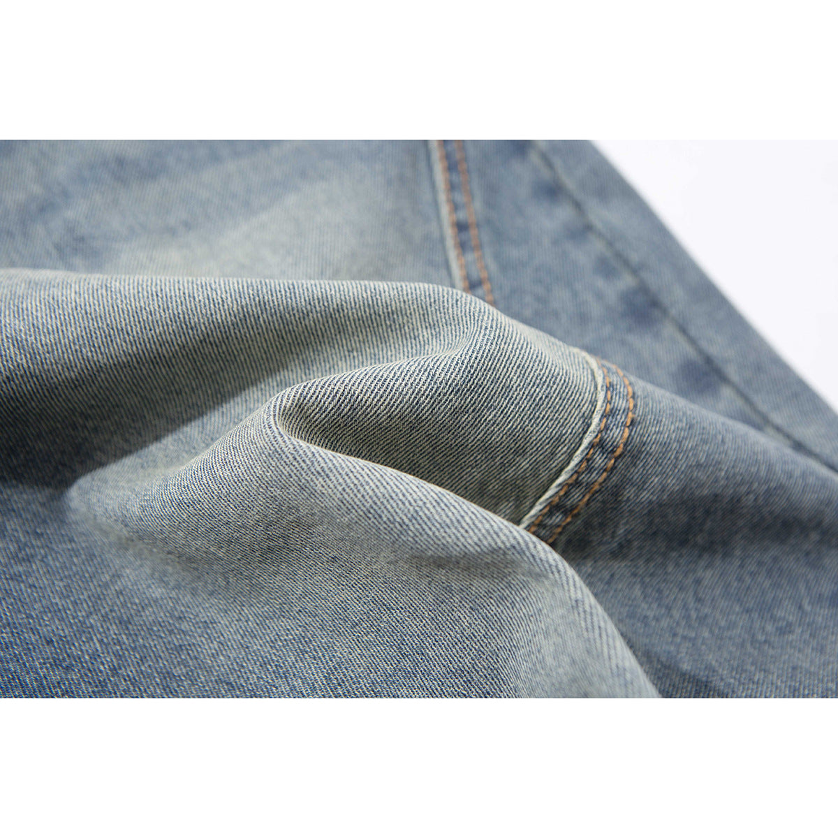 Close-up of blue denim fabric folded to show its diagonal weave and orange seam stitching.