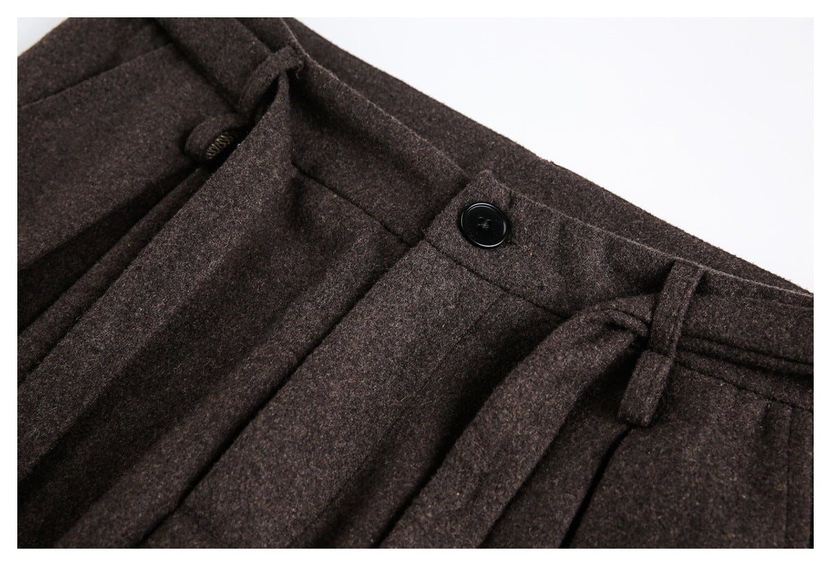 Close-up of dark brown trouser waistband with a black button, pleats, and belt loops.