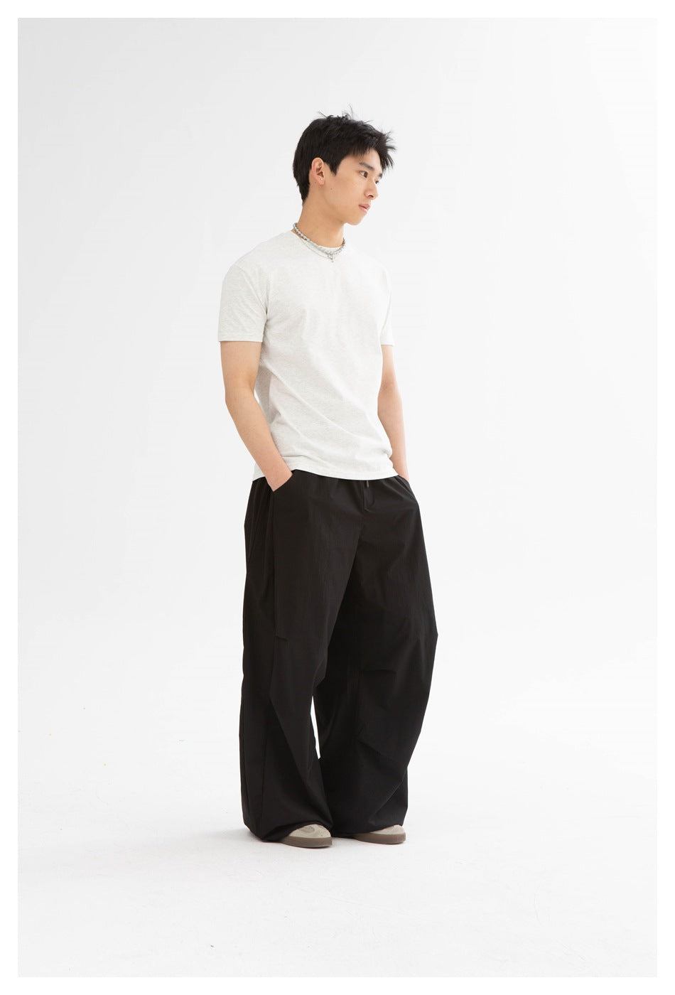 Three-quarter view of a model wearing a light heather-gray T-shirt and wide black pants.